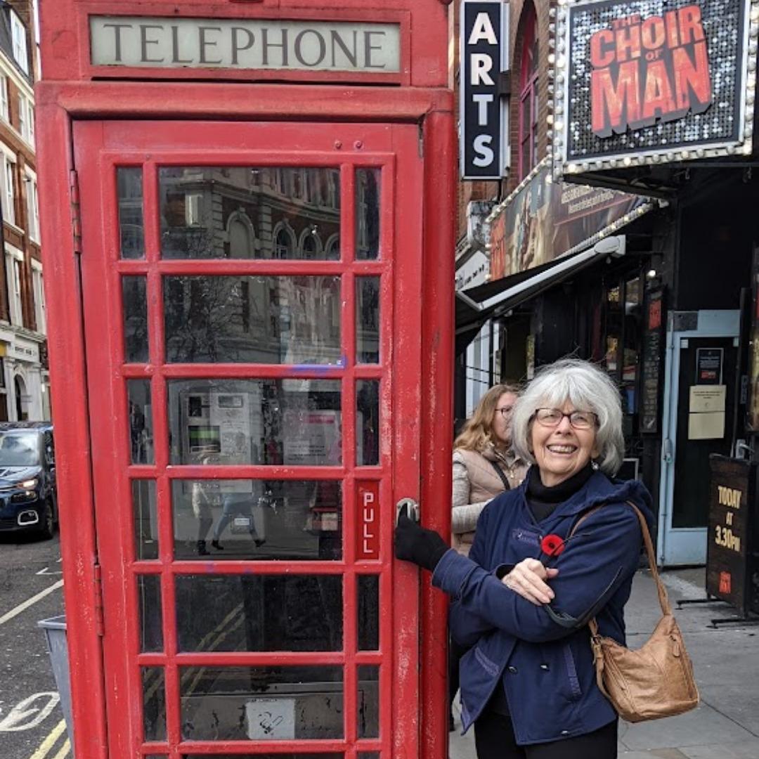 A woman standing in front of an iconic red London phone booth.