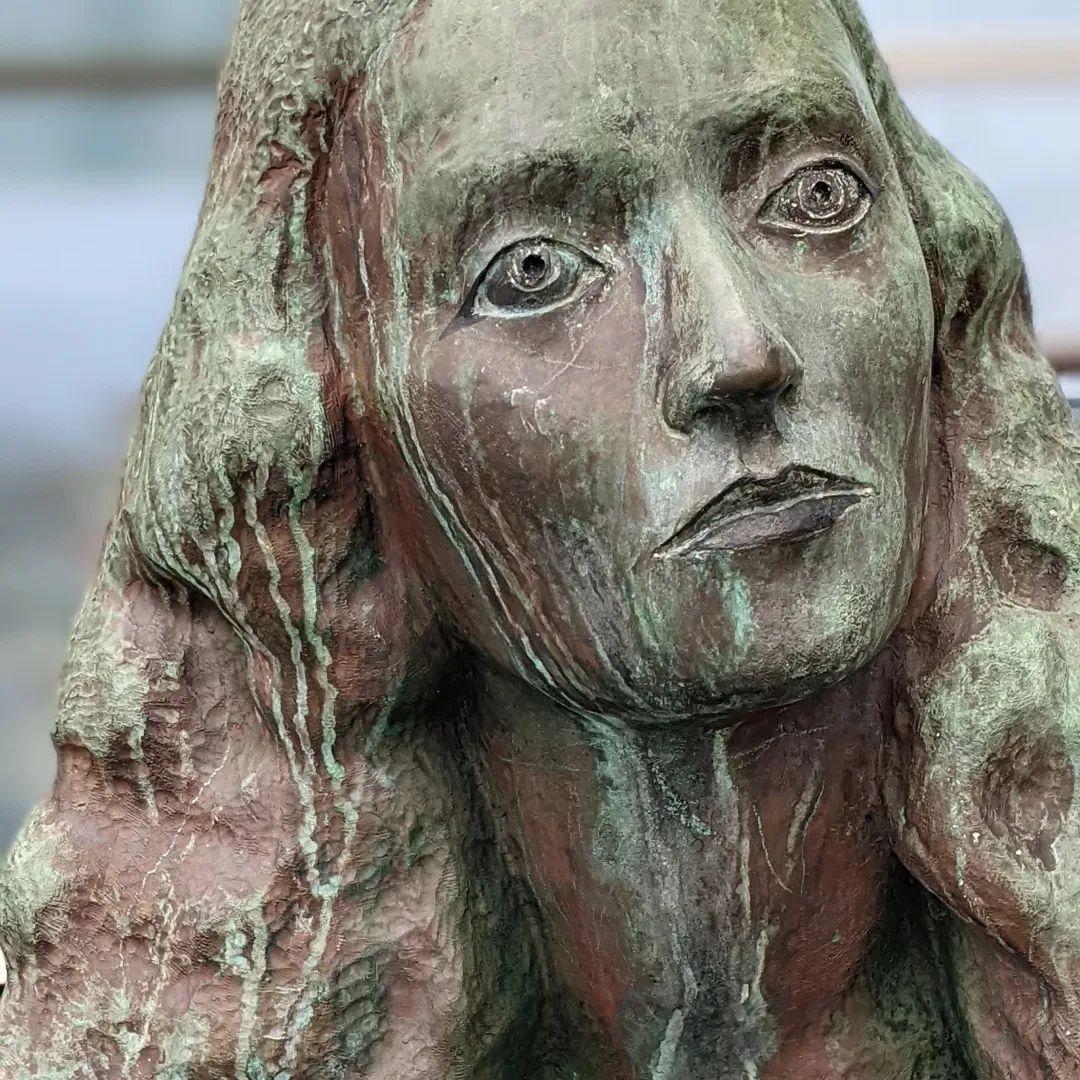 Close up of a bronze statue of a woman's face.  There are a lot of green oxydation streaks